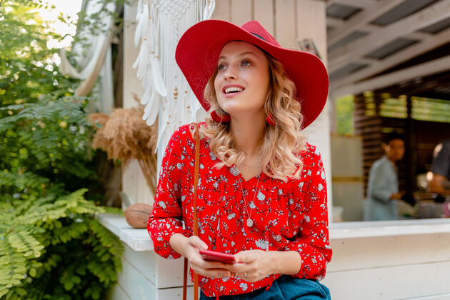 情感迷人的时尚金发微笑的女人在稻草红帽子和衬衫夏季时尚服装举行使用智能手机咖啡厅年轻脸女人