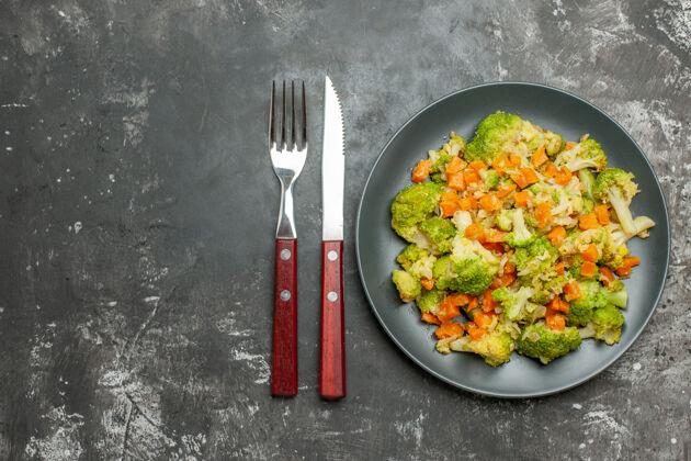 特纳健康餐 黑盘子上放花椰菜和胡萝卜 灰色桌子上放刀叉厨具叉子晚餐