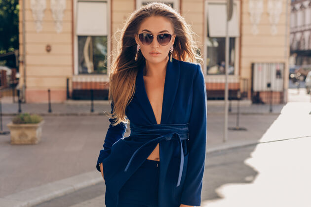 富有在阳光明媚的秋日 穿着蓝色西装戴着墨镜走在街上的性感时尚女人的画像姿势时尚现代