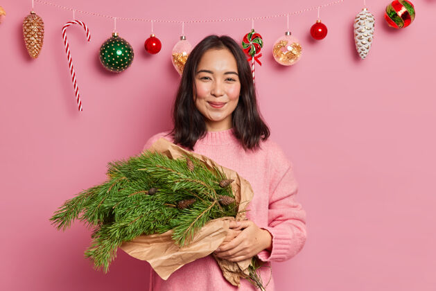高兴梦幻快乐的亚洲女人手拿着用绿云杉树枝做成的手工新年花束 穿着休闲套头衫 为寒假做准备制造亚洲冷杉