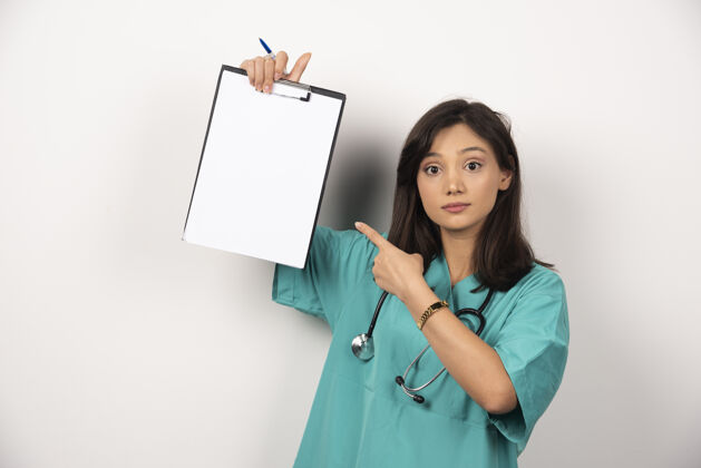 妇女女医生用听诊器指着白色背景上的剪贴板保健持有医院