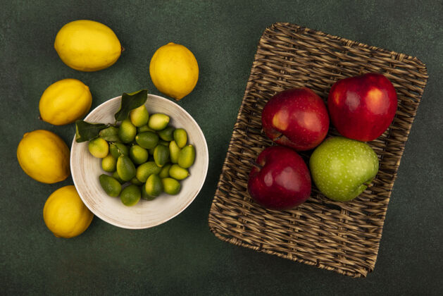 新鲜新鲜五颜六色的苹果放在柳条托盘上 金盏花放在碗里 柠檬孤立在绿色的表面上水果柳条特写