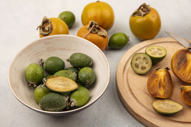 柿子一碗新鲜的柿子和一块灰色表面的木制厨房板上的柿子的俯视图板食物碗