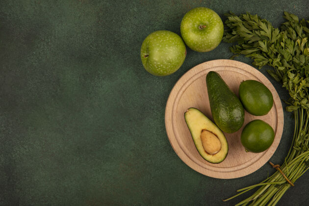 皮绿色皮肤的鳄梨俯视图在一个木制的厨房板与青苹果和欧芹柠檬隔离在一个绿色的表面与复制空间木材蔬菜厨房