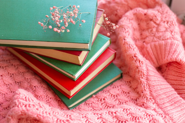 封闭一堆红绿相间的书 粉色温暖的针织毛衣上挂着干花知识开花房子