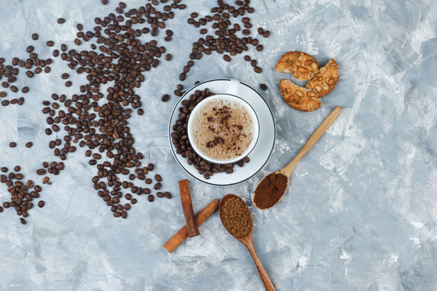 质地咖啡杯里有饼干 咖啡豆 磨碎的咖啡 肉桂棒 灰色石膏背景的顶视图烤粗麻布浓缩咖啡