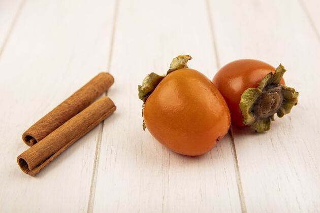 美味新鲜多汁的柿子与肉桂棒隔离在一个白色的木制表面俯视图柿子营养水果