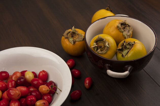 营养白色碗上的茱萸樱桃顶视图 木制表面碗上的黄色柿子水果配料健康饮食