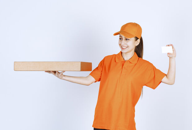 预订身着橙色制服的女快递员手持外卖披萨盒 出示名片快速智能货物