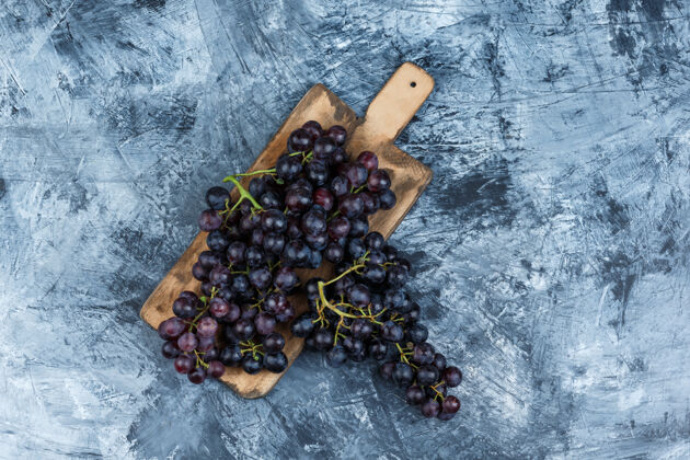 葡萄藤把黑葡萄平放在肮脏的灰泥和砧板背景上水平切割水果素食