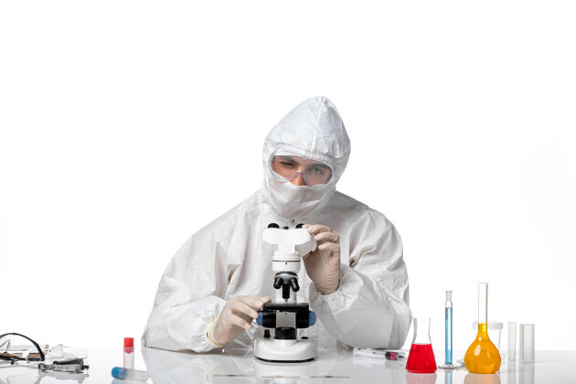 药品正面图：男医生穿着防护服 戴着口罩 在白色办公桌上使用显微镜男医生病毒正面