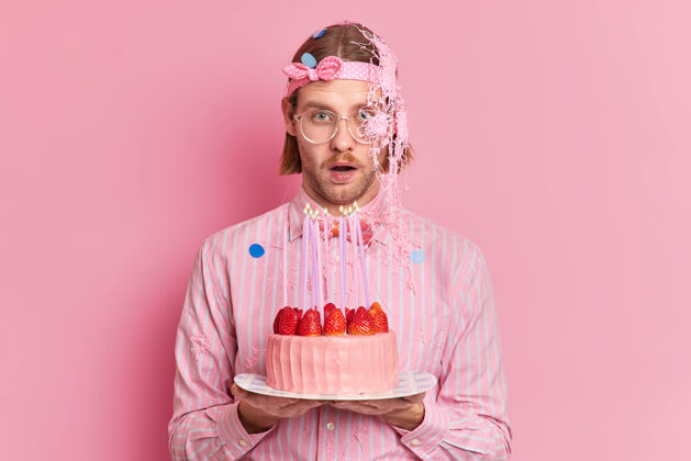 庆祝印象深刻的白种人对一些令人惊讶的事情作出反应庆祝生日去吹蜡烛和许下愿望穿着优雅的衣服隔离在粉红色的墙上眼镜草莓聚会