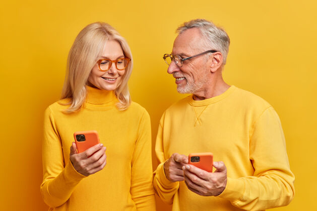 聊天快乐的老两口在家里用手机谈笑风生穿着休闲服对着鲜艳的黄色墙壁摆姿势站欧洲男性