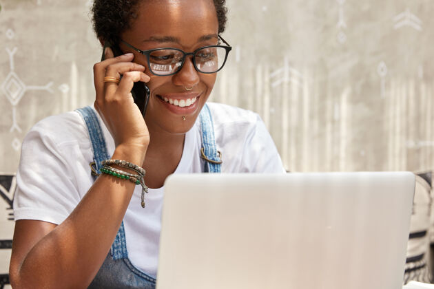 通信成功的年轻女经理在笔记本电脑上工作时通过智能手机打电话专业文件美式