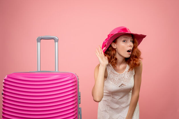 旅行戴着粉红色帽子和包的年轻女游客的正面图 在粉红色的墙上聆听情感欢呼美丽