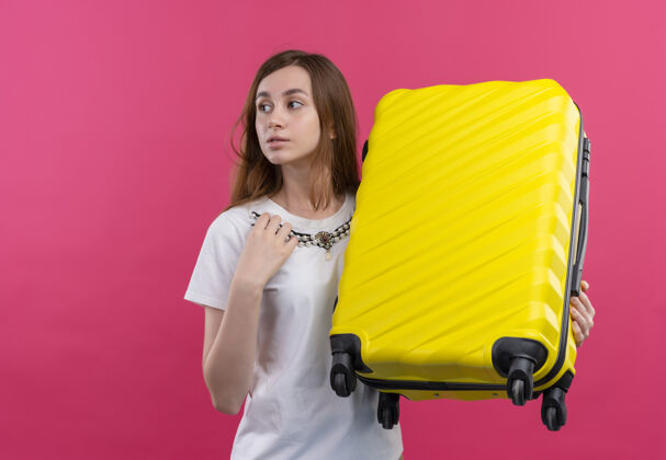手提箱体贴的年轻旅行家女孩拿着手提箱 把手放在胸前 看着左边的粉红色墙壁 还有复印空间年轻人手壁板