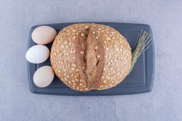 烘焙食品三个鸡蛋一条面包和一根麦秆放在大理石表面的木板上配料面包面粉