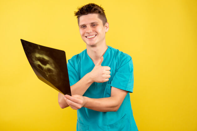 人正面图身穿医疗服的年轻男医生拿着黄色背景的x光片X光医学医院