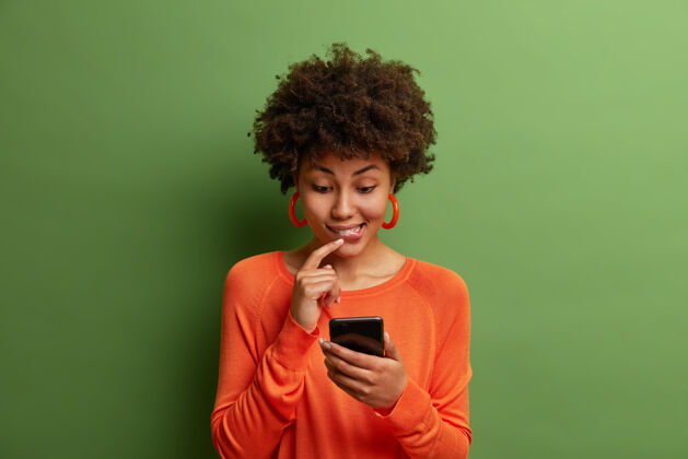 评论通讯 科技 生活理念好奇的黑皮肤女人在网上看有趣的帖子 手里拿着手机 想着如何在收到的信息上给出答案 在室内摆姿势电话绿色民族