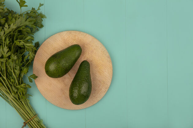 食物新鲜鳄梨的顶视图在一个木制的厨房板与欧芹隔离在一个蓝色的墙壁与复制空间午餐素食美食