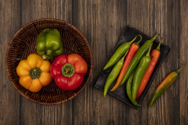 蔬菜黑色盘子上的新鲜长辣椒和木桶上的甜椒的顶视图木料餐辣