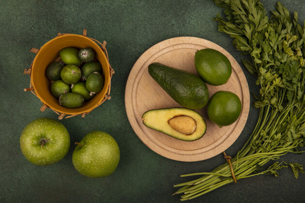 午餐木料菜板上的鳄梨俯视图 桶上放着酸橙 绿色的苹果和欧芹 隔离在绿色的墙上美食食物肥肉