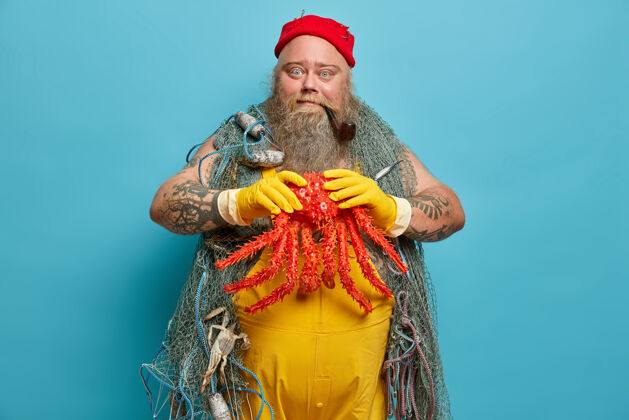 钓鱼熟练的大胡子渔夫手里拿着用渔网钓到的大章鱼 在港口摆姿势 戴着黄色的橡胶手套英俊章鱼水手