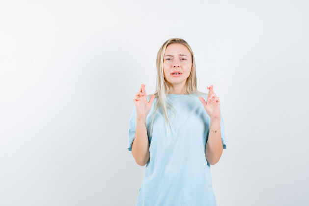 交叉年轻女士在t恤衫上交叉手指 看起来充满希望 正面视图手指微笑护理