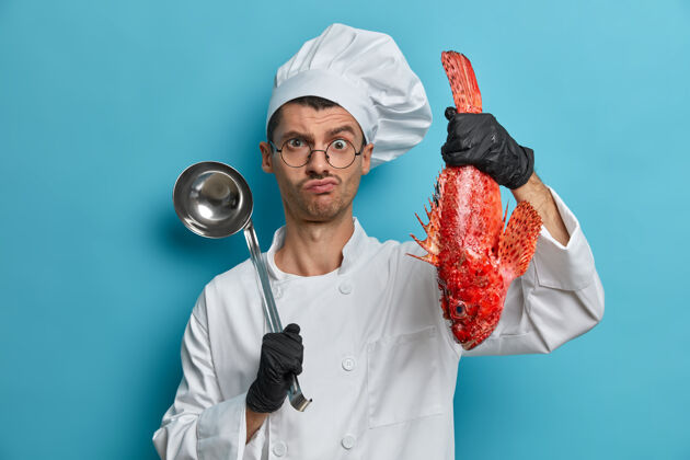 面部严肃的专业厨师拿着勺子和鱼 准备美味的海鲜菜肴 穿着白色制服 戴着黑色手套 煮红鲈鱼汤室内营养年轻
