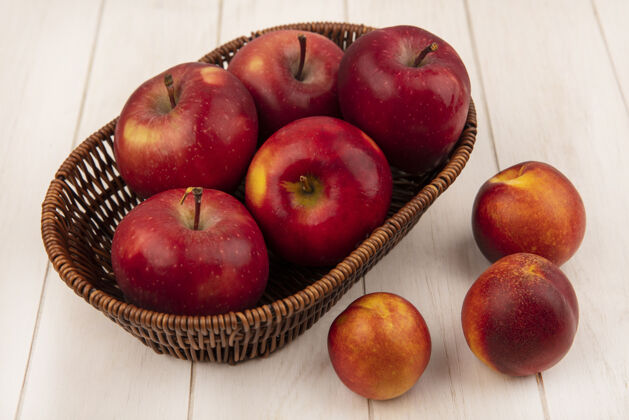 中心在白色的木墙上 一个桶上放着甜的红苹果 里面的桃子被隔离开来等级桶农业
