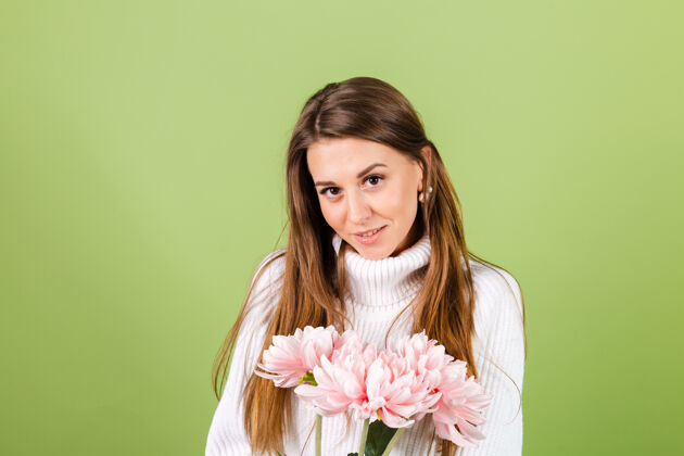 成人漂亮的欧洲女人穿着休闲的白色毛衣孤立 浪漫的样子拿着一束粉红色的花微笑着开花庆祝祝贺
