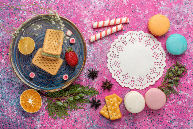 顶视图俯瞰美味的华夫饼 在粉红色的表面上放上一杯茶和麦卡龙华夫饼粉末饼干