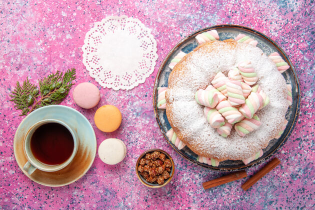 糖粉红色桌子上的糖粉蛋糕和一杯茶和法国马卡龙的俯视图生的麦卡龙茶