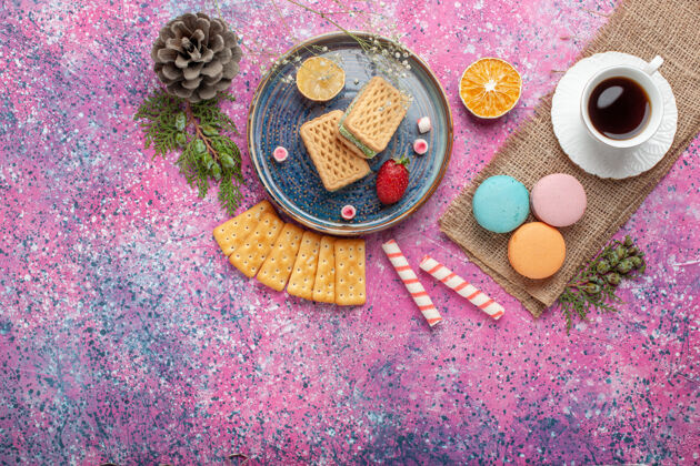 美味美味的华夫饼与法国马卡龙和粉红色表面上的茶俯瞰图胭脂庆典五颜六色