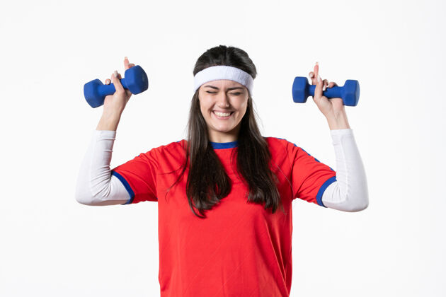 人正面图微笑的年轻女性穿着运动服 用哑铃锻炼身体球员前面视图
