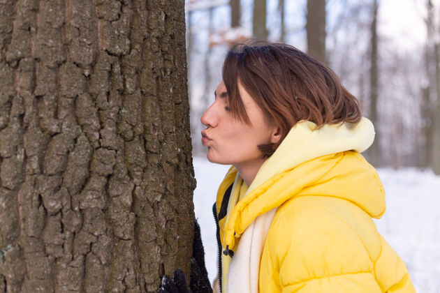 人美丽的年轻女子在冬天的森林里表现出对大自然的柔情 表现出对树的爱树亲吻公园