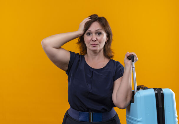 手势未出租的中年旅行妇女拿着手提箱 把手放在孤立的桔子头上旅行者不愉快手
