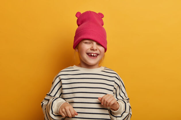 玩真挚感性的孩子玩着新帽子 穿着条纹套头衫 笑着欢呼着什么 有着搞笑快乐的表情 嬉戏的心情 发疯了 孤立在充满活力的黄墙上有趣狐狸童年