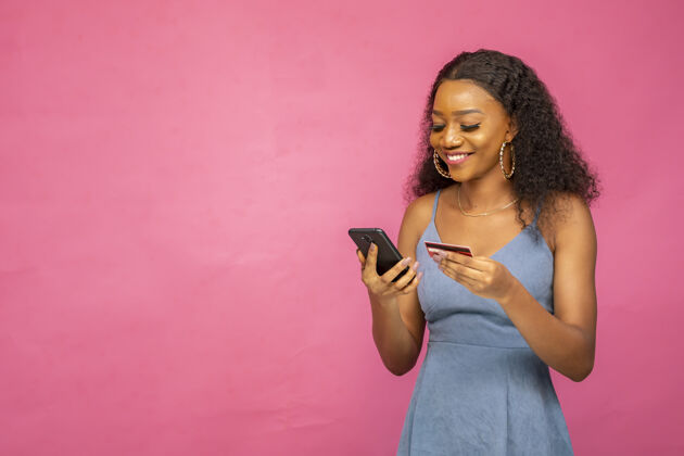 支付年轻漂亮的非洲女人用她的手机和信用卡喜悦微笑女人