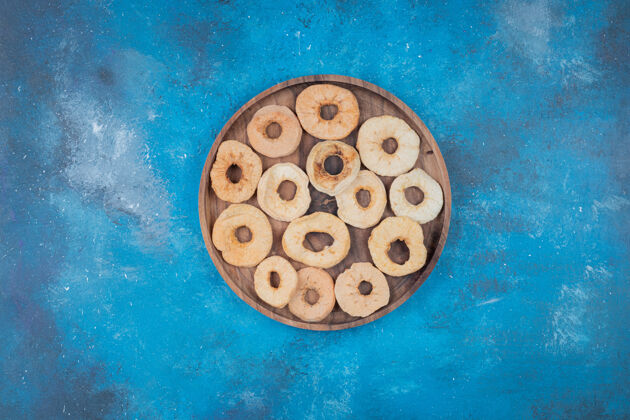 染色干苹果片放在蓝色表面的木板上零食食物脱水