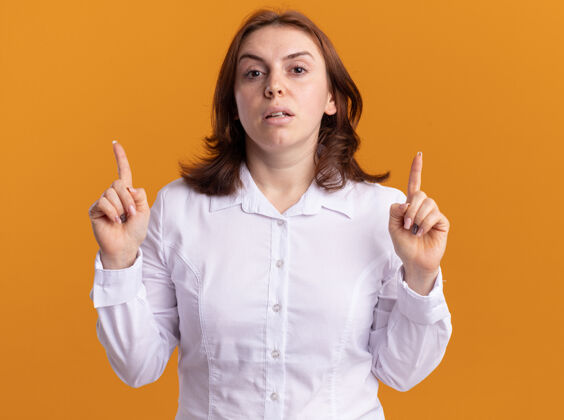 指着身穿白衬衫的年轻女子严肃地看着前面 食指朝上 站在橙色的墙上吹牛衬衫脸