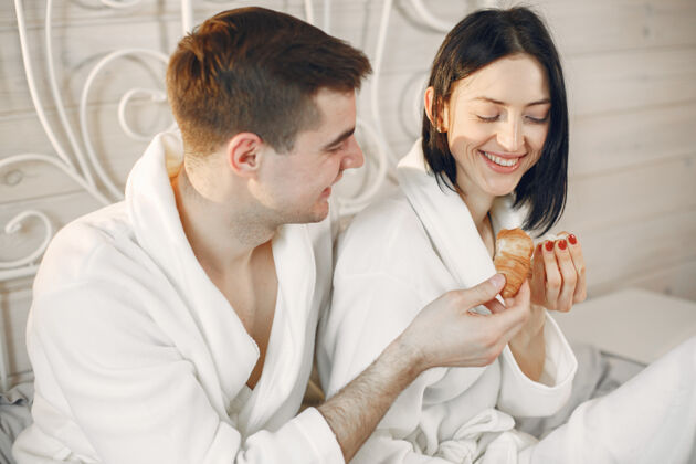 男人可爱的情侣穿着浴衣在卧室里吃早餐欢呼浴袍休闲