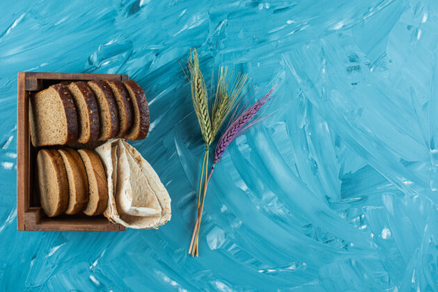 木头一个木箱 里面装着蓝色背景的棕色新鲜面包片和小麦穗美味食物谷类食品