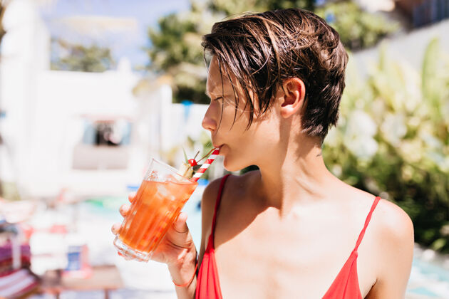 成人一个留着时髦发型的无忧无虑的女孩在度假胜地喝着水果鸡尾酒欧洲泳装快乐