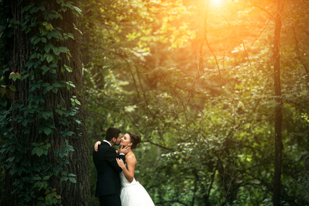 外面美丽的新婚夫妇在森林里摆姿势拥抱男人羽毛