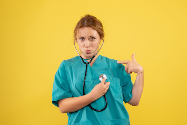 医疗器械黄色墙壁上穿着带听诊器的医疗服的女医生的正视图医疗医生病毒