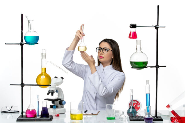 桌子前视图穿着白色医疗服的女化学家正在白色办公桌上处理科维德科学大流行实验室病毒的解决方案医生工作人