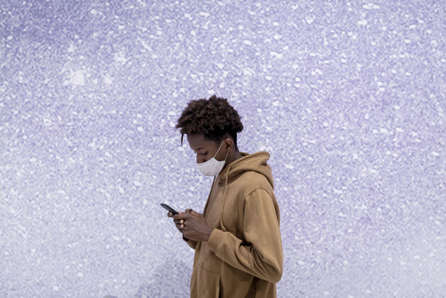 数字设备一个年轻人在紫色的闪光墙边用他的手机非洲裔美国人男孩男人