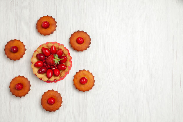饼干俯瞰白色书桌上美味的小蛋糕框架浆果花