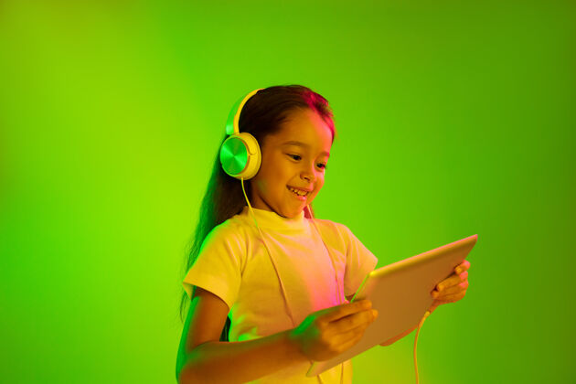 面部美丽的女性半身像 隔离在霓虹灯下的绿色背景上年轻感性的女孩人类情感 面部表情概念时尚的颜色使用平板电脑进行游戏 虚拟博客 自拍人海洋孩子